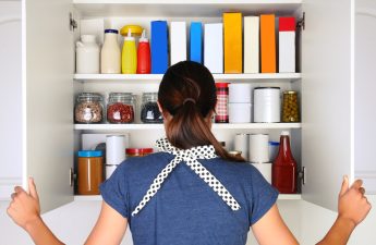 Woman seen from behind opening food cupboards.